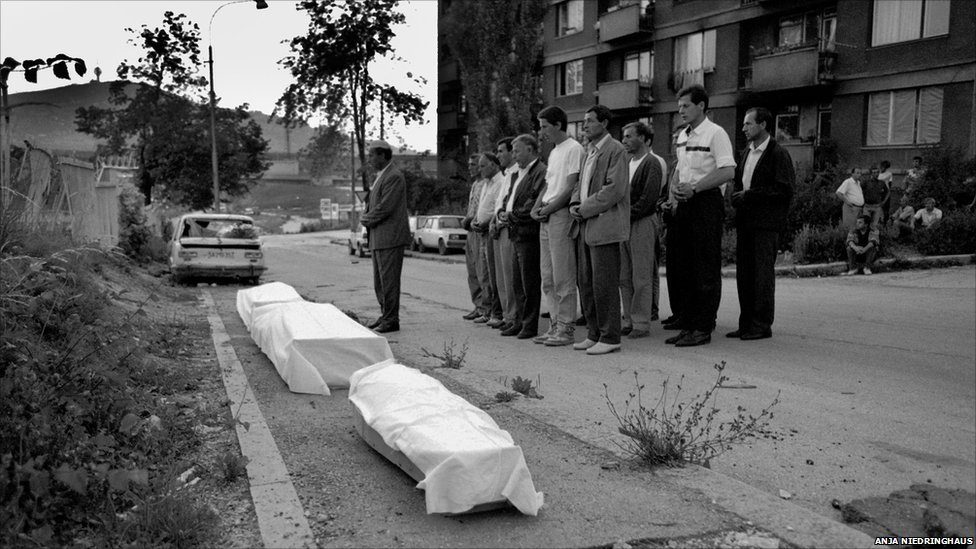 Bosnian Muslim men attend a funeral ceremony at sunset to be more protected from sniper fire. Sarajevo. July 20, 1993. Many times funeral ceremonies came under sniper fire with people taking cover in ditches next to coffins. At this funeral, three Muslim family members - two brothers and their mother - were to be buried. The men arrived at sunset and placed the coffins on the street next to Sarajevo’s Lion Cemetery since the surrounding buildings gave more cover against sniper fire. After the funeral ceremony, the coffins were buried in darkness. EPA/ANJA NIEDRINGHAUS