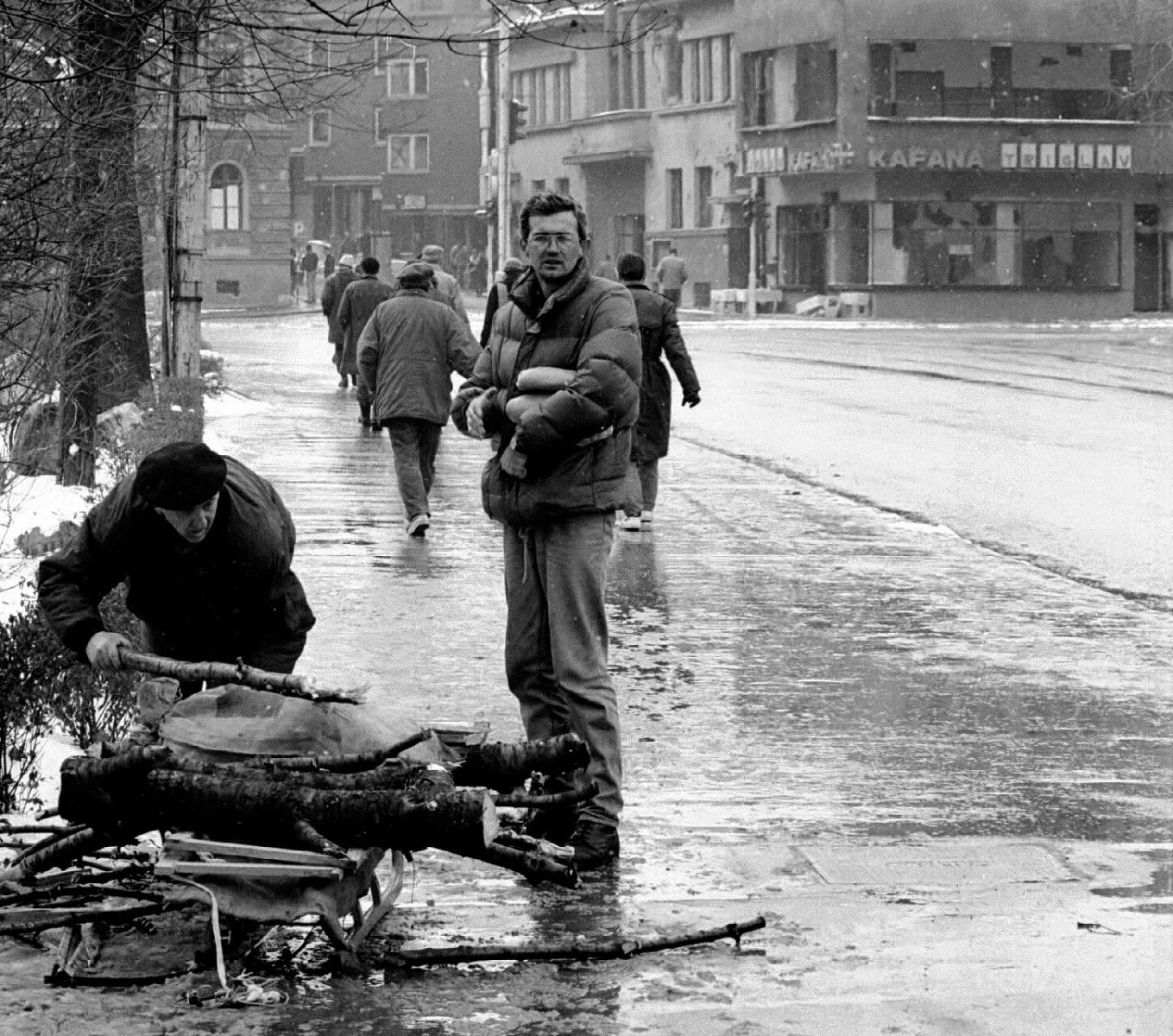 Stooped man loads his sled with sawn and scavenged firewood. Never enough in the bitter cold. Standing man carries two precious loaves.