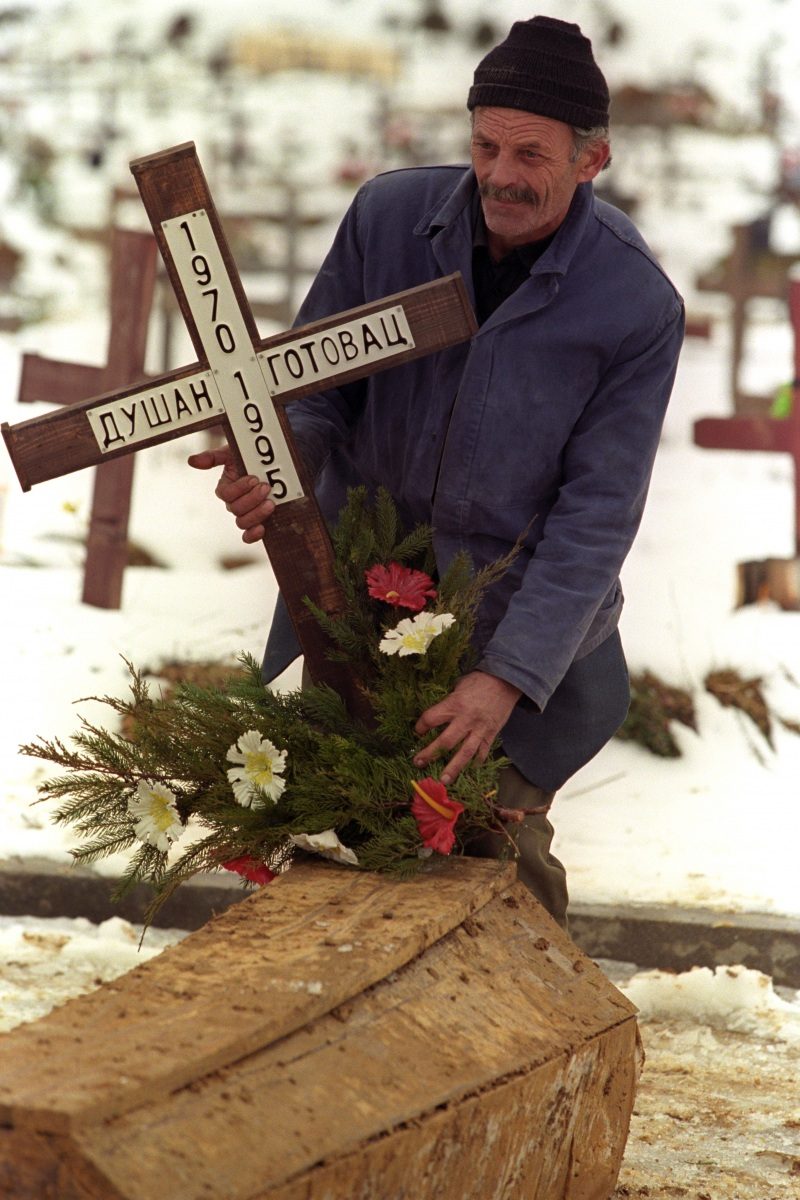 A cemetery worker fixes a large crucifix alongside the coffin of a 25-year-old victim. Sarajevo, 15 February 1996. EPA | DIMITRI MESSINIS