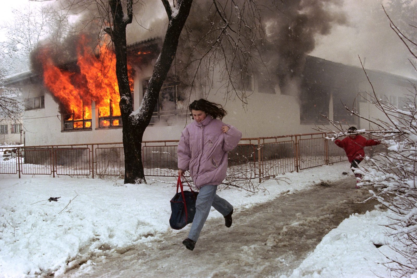 Woman and a child run, passing by the burning kindergarten in the suburb of Vogosca, Sarajevo, Bosnia And Herzegovina, 22 February 1996. EPA | DIMITRI MESSINIS
