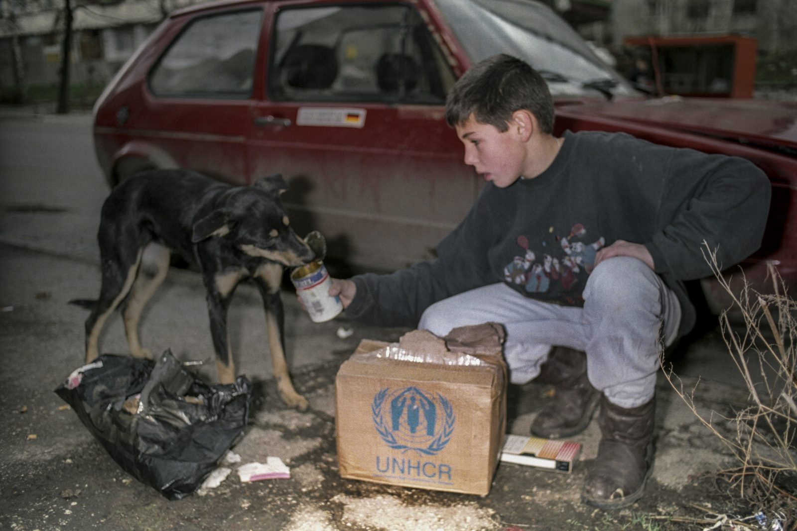 A boy feeds a hungry dog from a can after receiving some food from a humanitarian aid distribution in Sarajevo, 5 December 1992. EPA | DIMITRI MESSINIS