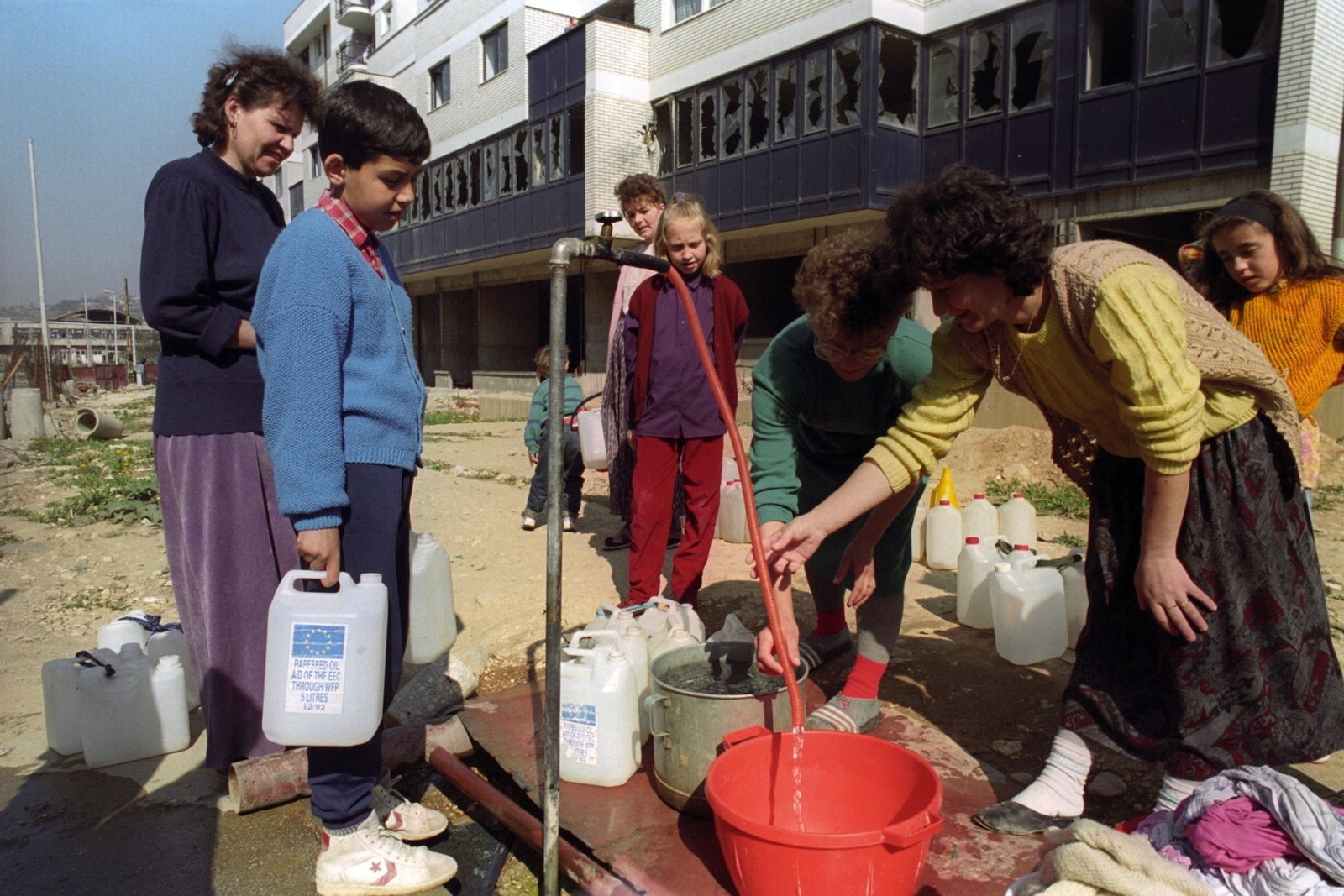 Mothers and children gather around an improvised water source to collect water for washing, cleaning and cooking in Sarajevo, Bosnia and Hercegovina, 22 April 1993.