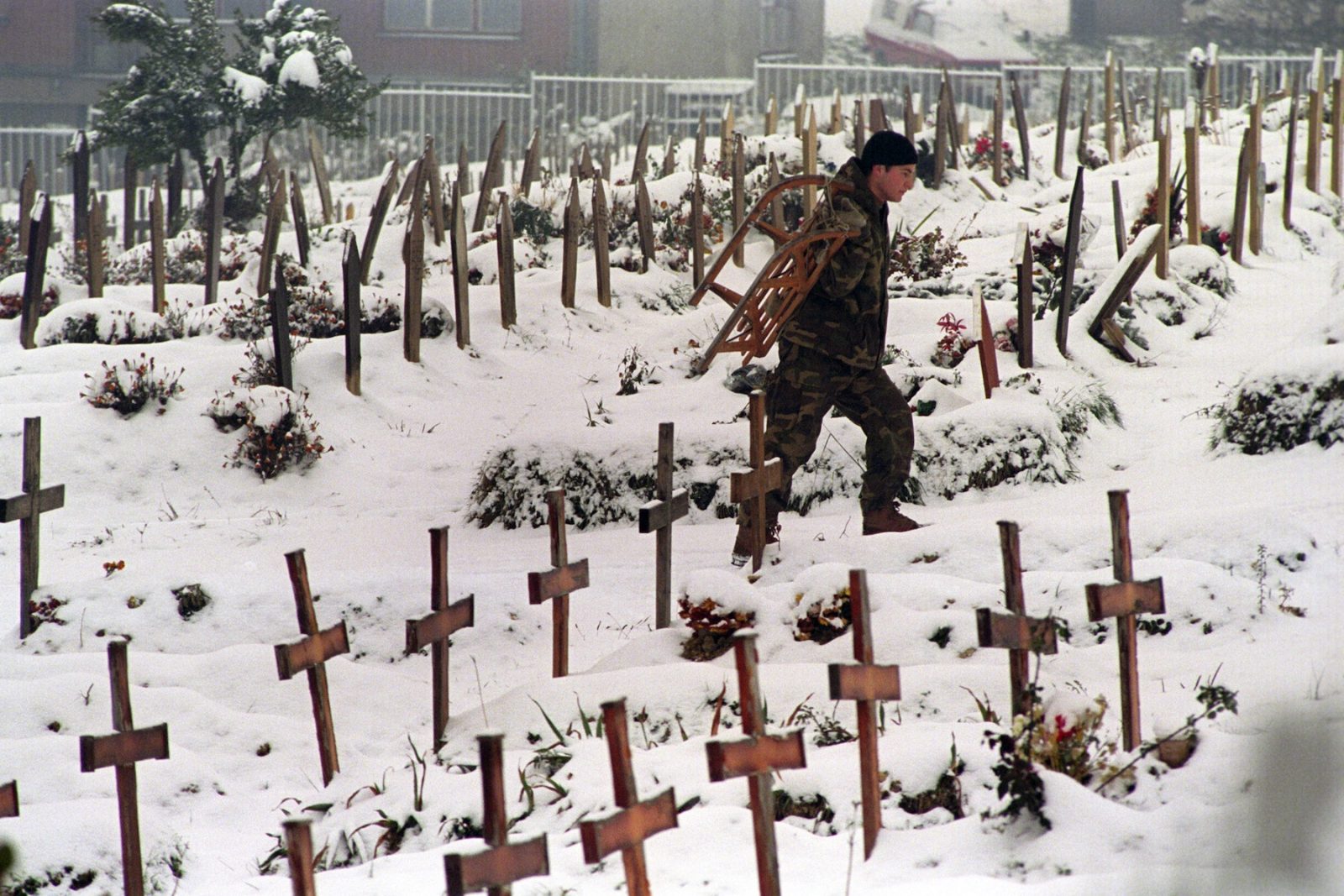 A man carries a sledge on his back as he walks through a snow-covered cemetery in Sarajevo, Bosnia and Hercegovina, 27 December 1993.