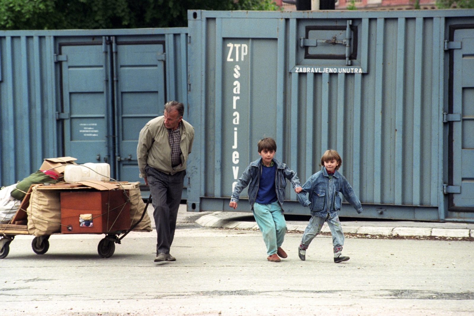 A boy holds onto his young sister as his father pulls a trolley of furniture and other belongings in Sarajevo, Bosnia and Hercegovina, 21 May 1995.