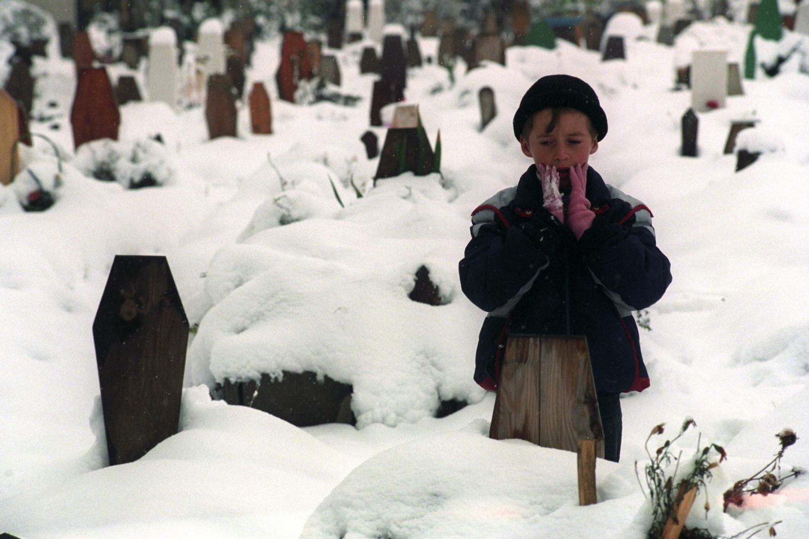A young boy prays in front of the grave of his father at a cemetery which is covered by recent snow in Sarajevo, Bosnia and Hercegovina, 16 November 1993.