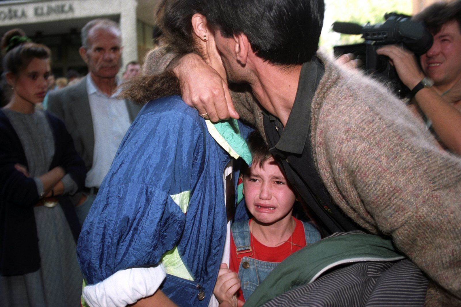 A young boy weeps while his parents kiss goodbye at a bus depot in Sarajevo, Bosnia and Hercegovina, 15 August 1993 as the father and husband returns to military duties.