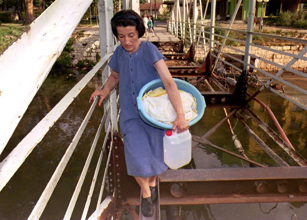 A Sarajevo resident makes her way across the remains of the Cumurija bridge carrying some laundry and a container of water 29 August 1993. Bosnia's three factions appear to be close to approving a peace plan and have agreed to return to Geneva for talks 30 Aug. (Photo by GABRIEL BOUYS / AFP)
