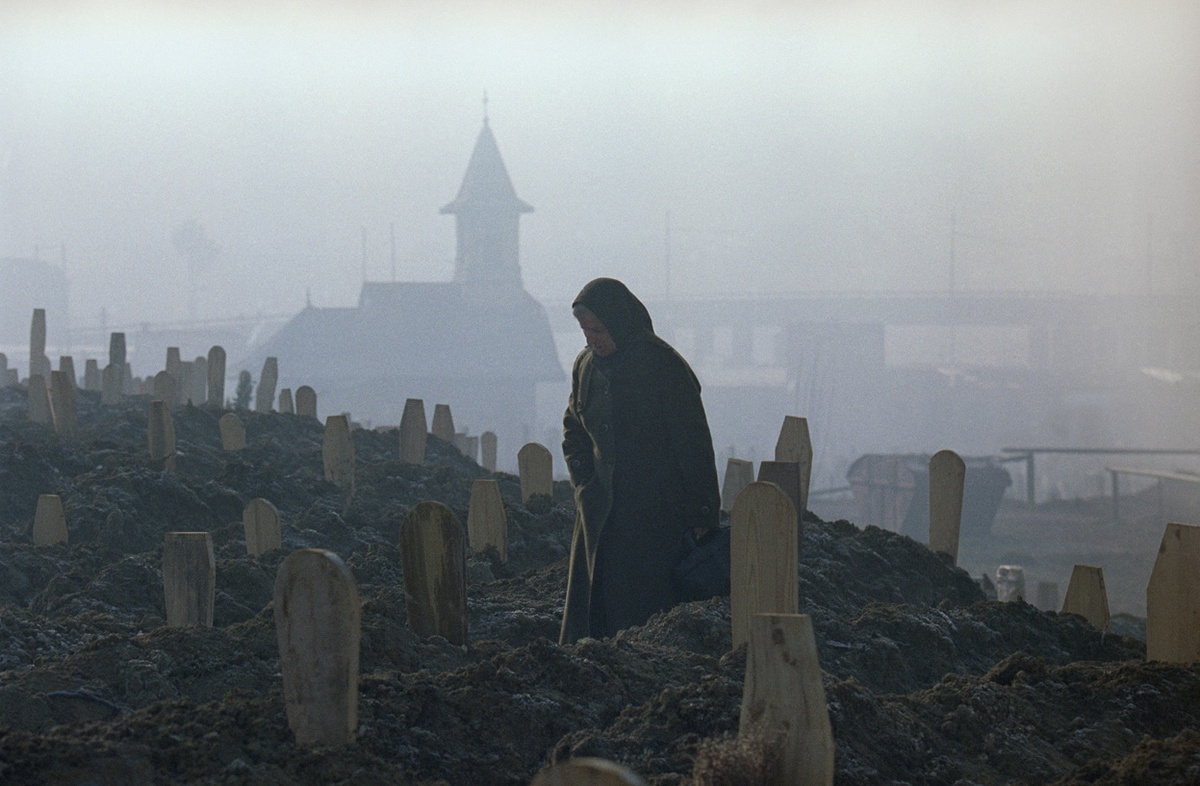 A woman, standing between markers of fresh graves in a Sarajevo cemetery, mourns over the grave of a dead relative in the early morning on 17 January 1993.