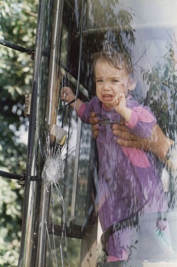 An unidentified orphan behind the damaged windshield of a bus in the town of Stup, near Sarajevo, on . A two-year-old Serbian girl and one-year-old Muslim boy were killed after a bus carrying them and 48 other orphans to safety away form Sarajevo was hit by heavy fire, officials said Sunday. The bus moved on to Split, Croatia.