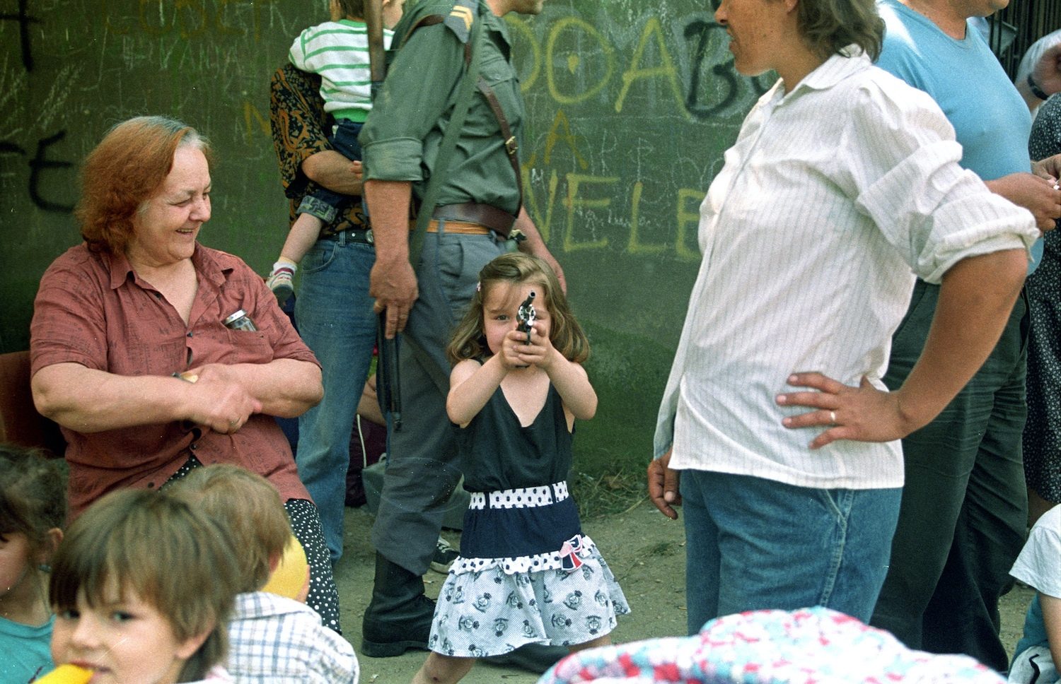 A girl plays with a gun, pointing at the photographer, in Sarajevo, August 12, 1992. During the siege of Sarajevo all roads leading in and out of the city were blocked, the airport was shut down. About 400,000 residents were trapped, and were cut off from all basic supplies. Thousands of civilians were killed and wounded, suffered from rape and starvation.