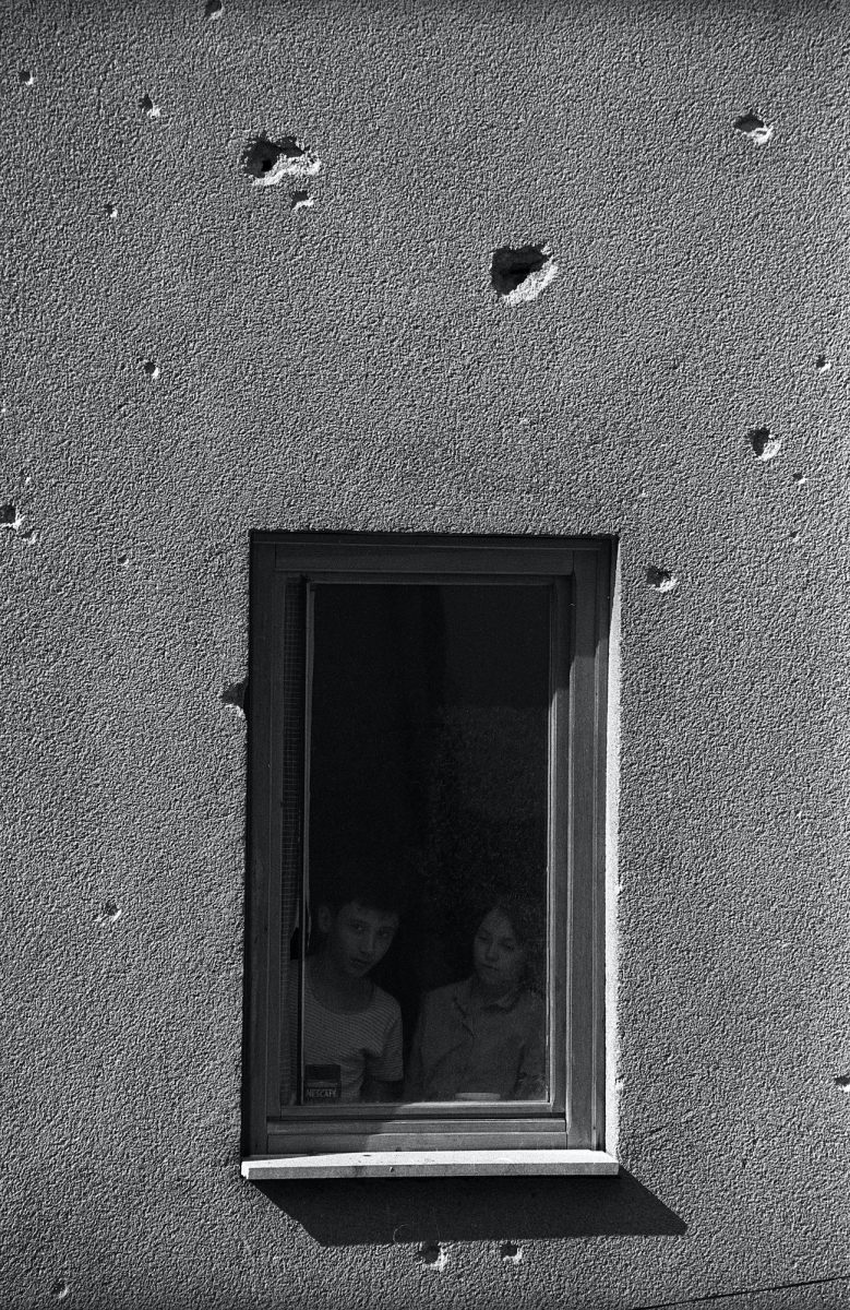 A couple of young kids looking outside their window during a bombing in the centre of Sarajevo. Sarajevo, Bosnia and Herzegovina, August 1993