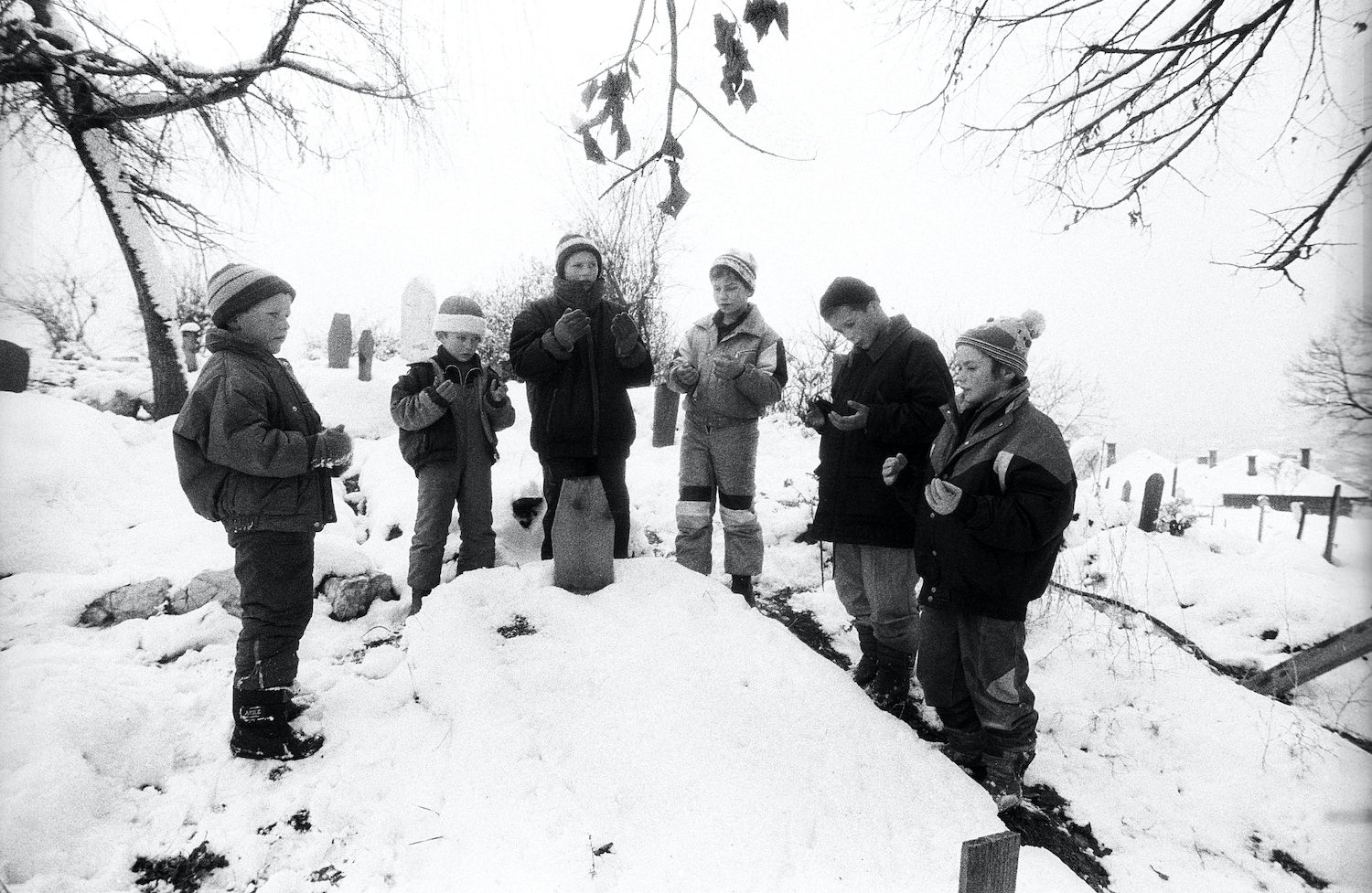 A group of young kids while praying in front of their friend’s grave died under a bombing. Sarajevo, Bosnia and Herzegovina, December 1994
