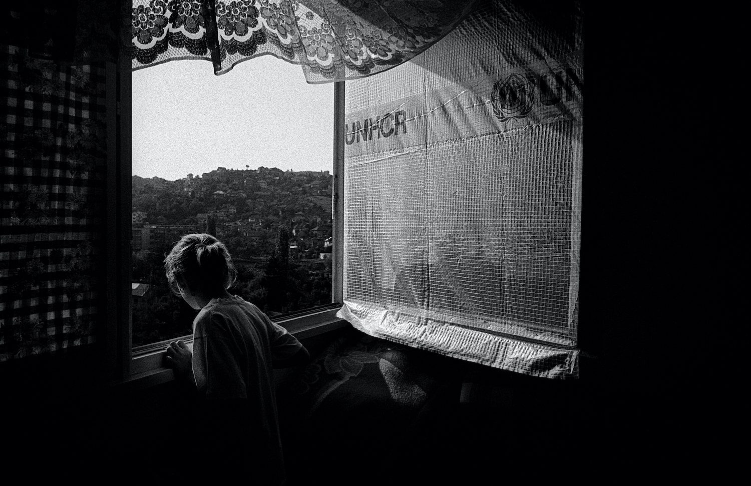 A young girl looks outside the window. Sarajevo, Bosnia and Herzegovina, July 1995