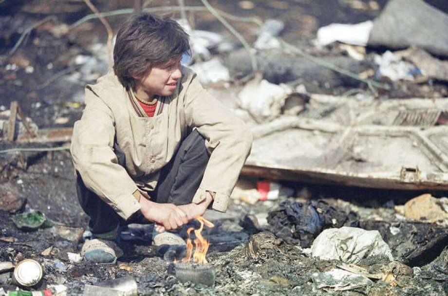 A boy tries to keep warm with a small fire in a trash dump in front of his house in Sarajevo on Wednesday, March 10, 1993.