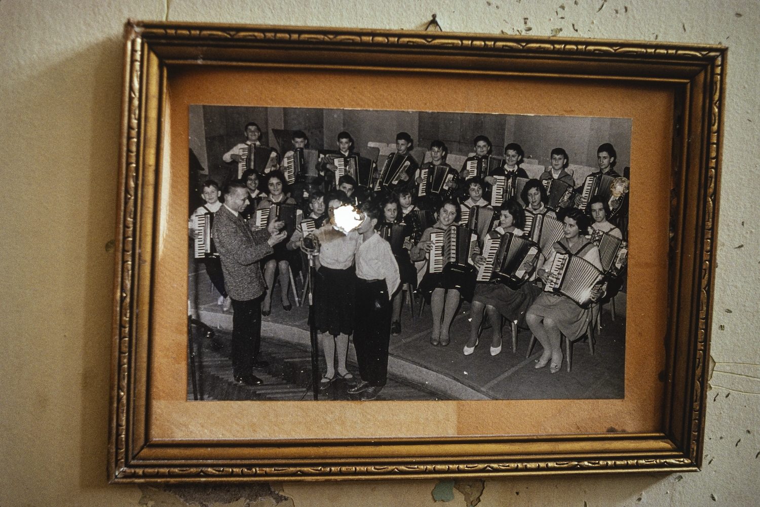 A bullet hole shot through a framed photograph of a youth accordion orchestra hanging on the wall in a school that marks the front line in the area of Gabivica controlled by Bosnian Serb soldiers, Sarajevo, September 1992