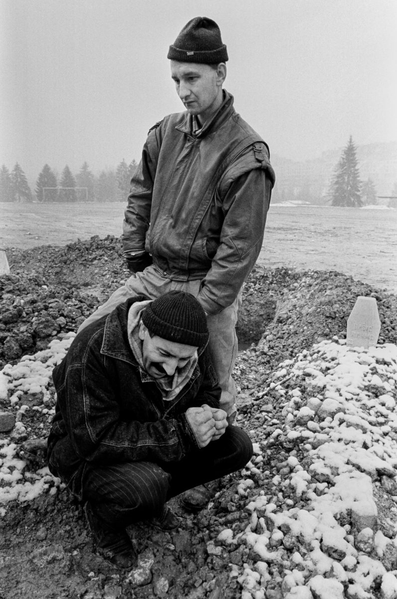 Two Bosnian men grieve at a friend's grave in a makeshift cemetery in a soccer field in Sarajevo on December 10, 1993.