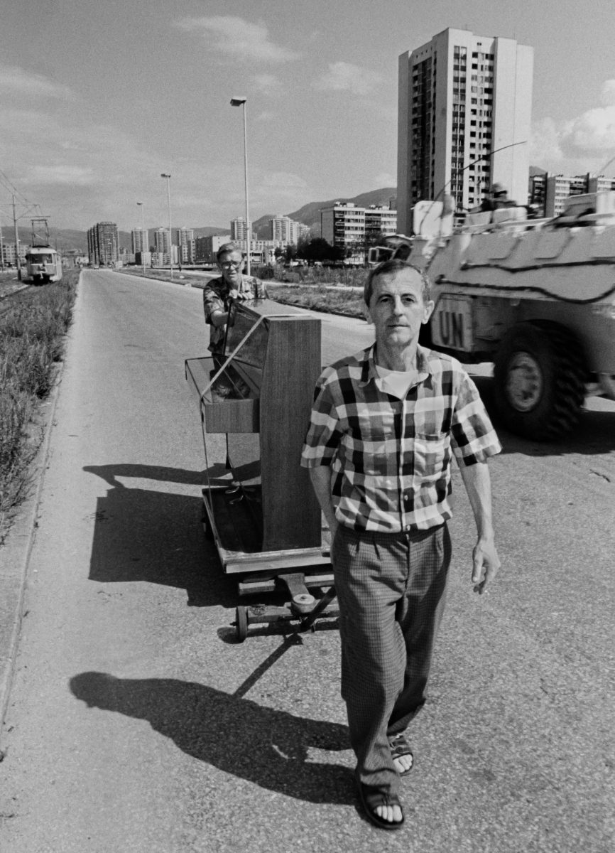 Two men move a piano along Sarajevo's notorious 'Sniper Alley' on August 30 1994, while a French United Nations armoured vehicle drives past.