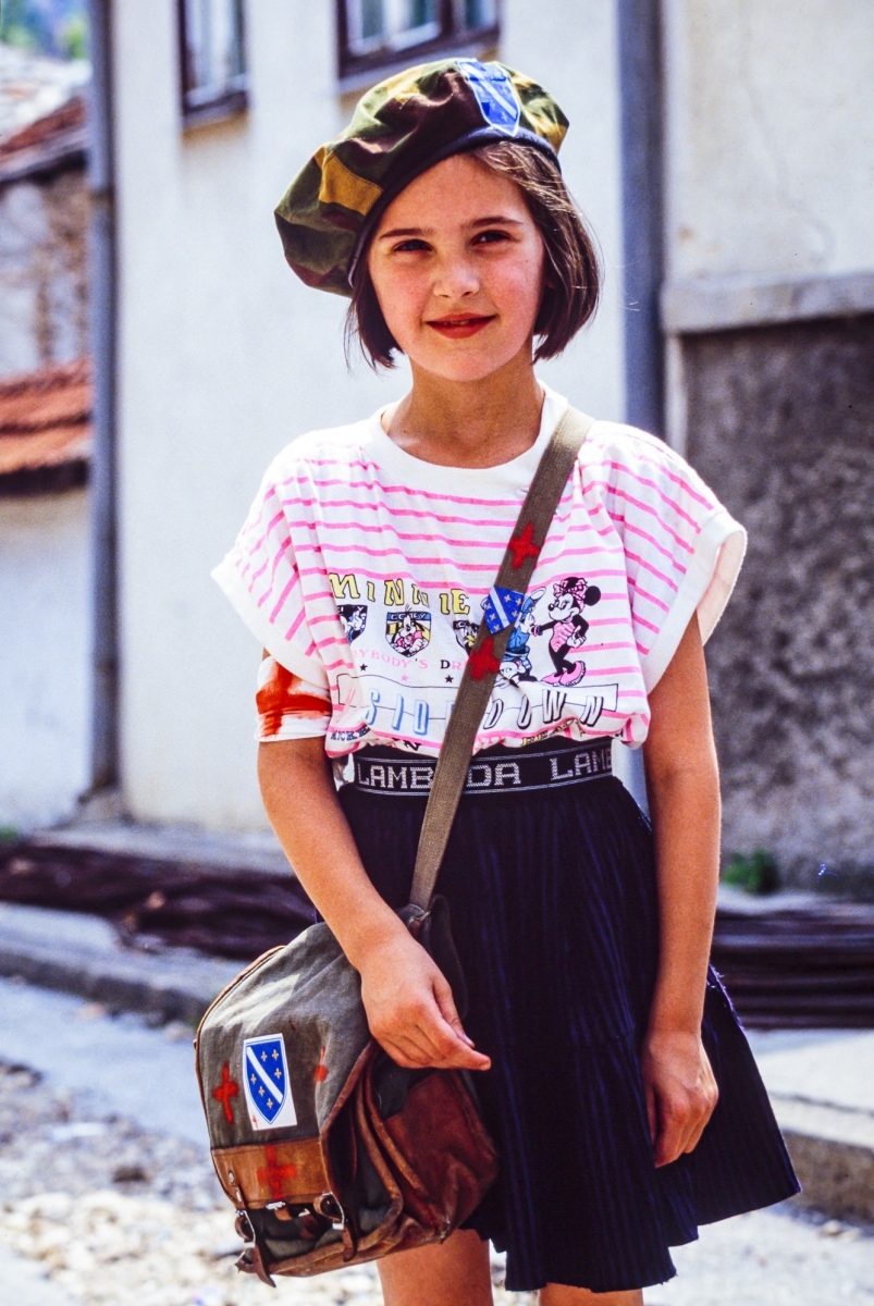 A young Bosnian girl wears a camouflage beret and shoulder bag decorated with patches of the Bosnian flag on the streets of Sarajevo. 27 July, 1992, Sarajevo, Bosnia and Herzegovina