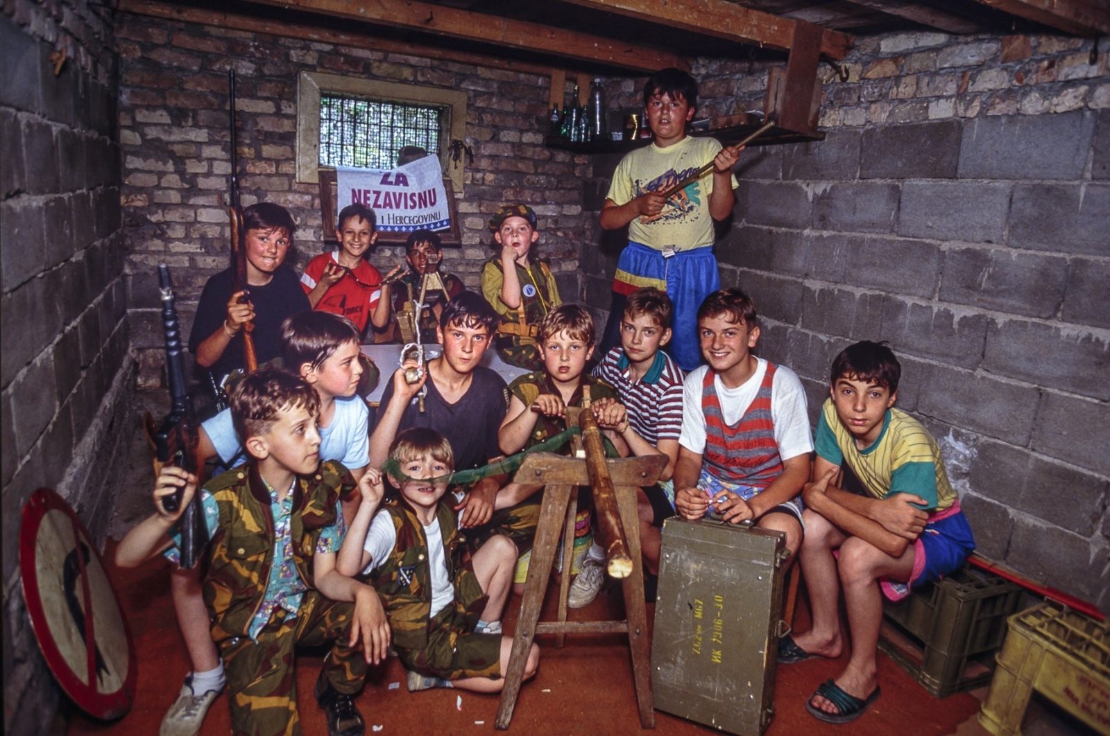 A group of Bosnian children, wearing camouflage military uniforms, play with toy weapons, including assault rifles, in a basement shelter. 27 Jul 1992, Sarajevo, Bosnia and Herzegovina