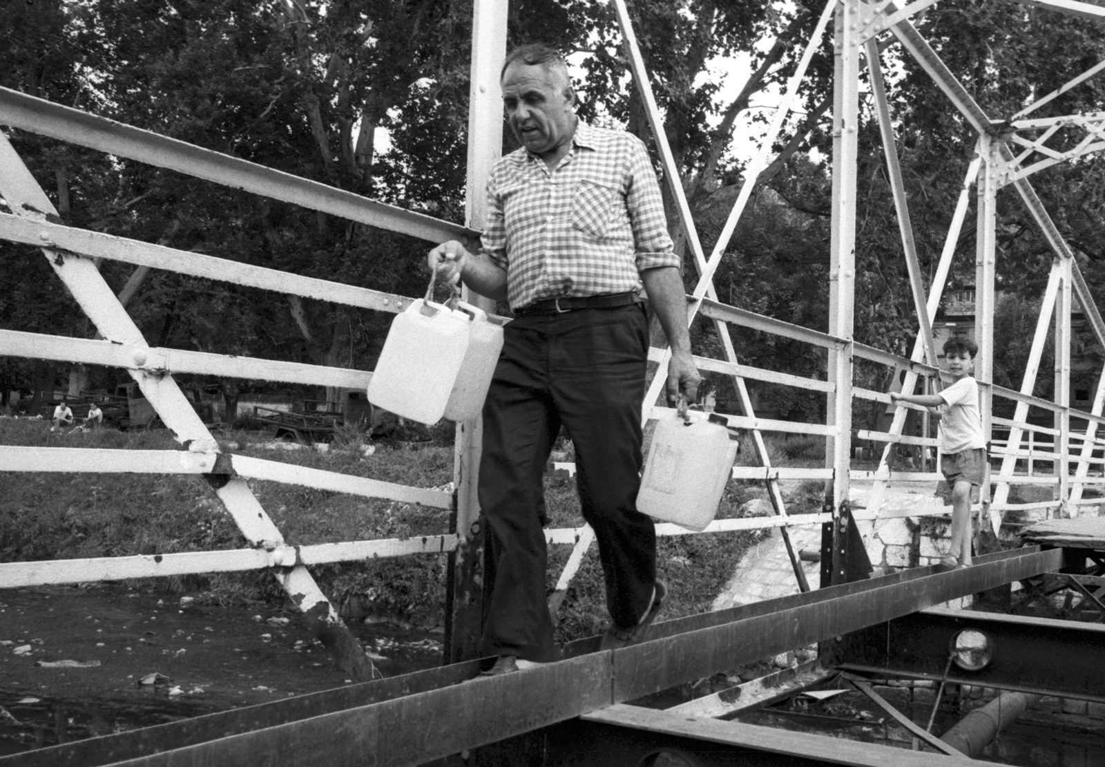 A man walks over the remains of a damaged bridge to collect water from a standpipe during the siege on Sarajevo by Serb troops.