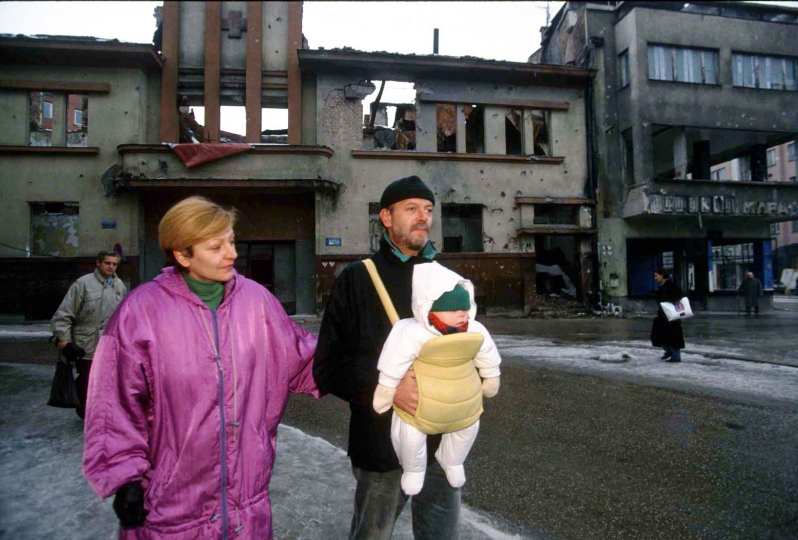 Parents walking with baby in baby carrier in front of destroyed buildings at the inter junction of Kranjceviceva Street and Marsala Tita Street. Sarajevo, January 1993. Photo Copyright © Peter Kullmann| Zone5 | fullframeRAW