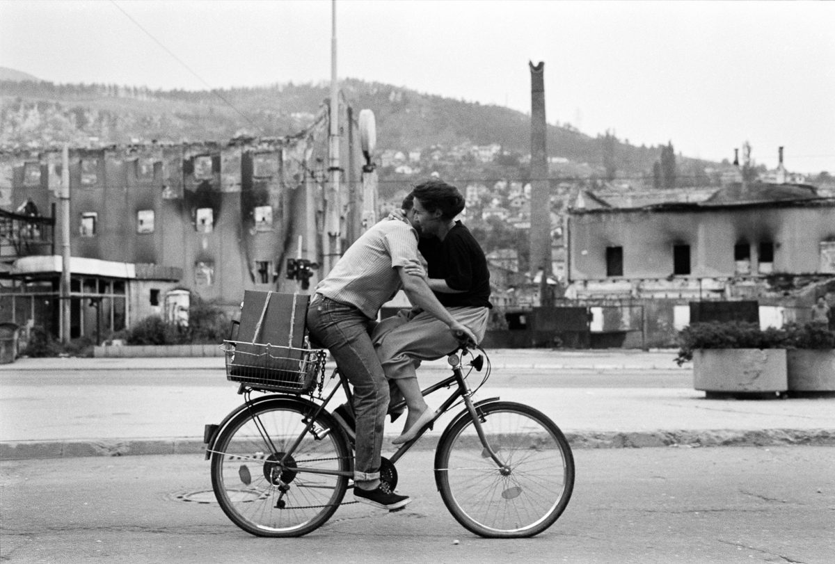 A couple shares a bicycle in wartime Sarajevo.