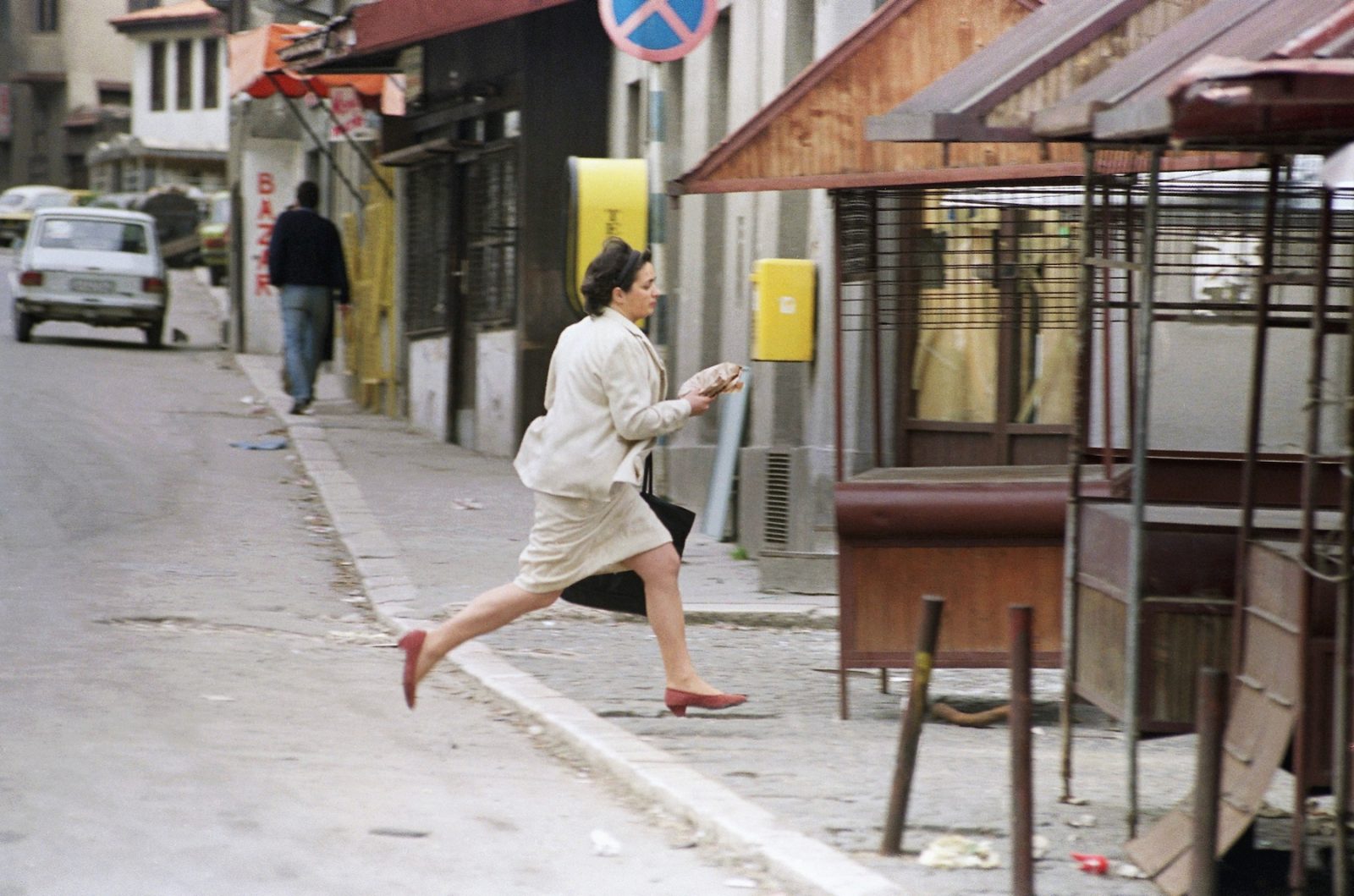A woman runs for cover past abandoned newspaper stands after a sniper opened fire on a main square in Sarajevo, Tuesday, May 12, 1992. Sporadic fighting continued in and around the city, as the European Community pulled its last observers out of Bosnia-Herzegovina, saying ethnic warfare made their mission too dangerous.