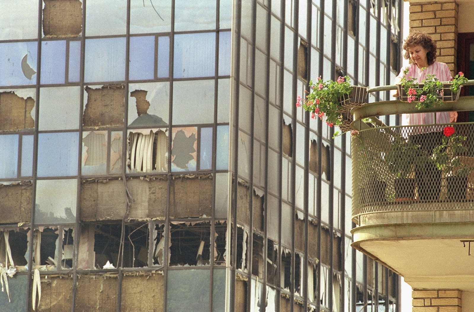An unidentified Sarajevo resident cleans her balcony on Sunday, June 7, 1992 in Sarajevo, after heavy fighting late Saturday caused heavy damage to the building in the background. Serbian forces continue to shell the town and Bosnian troops respond with fire.