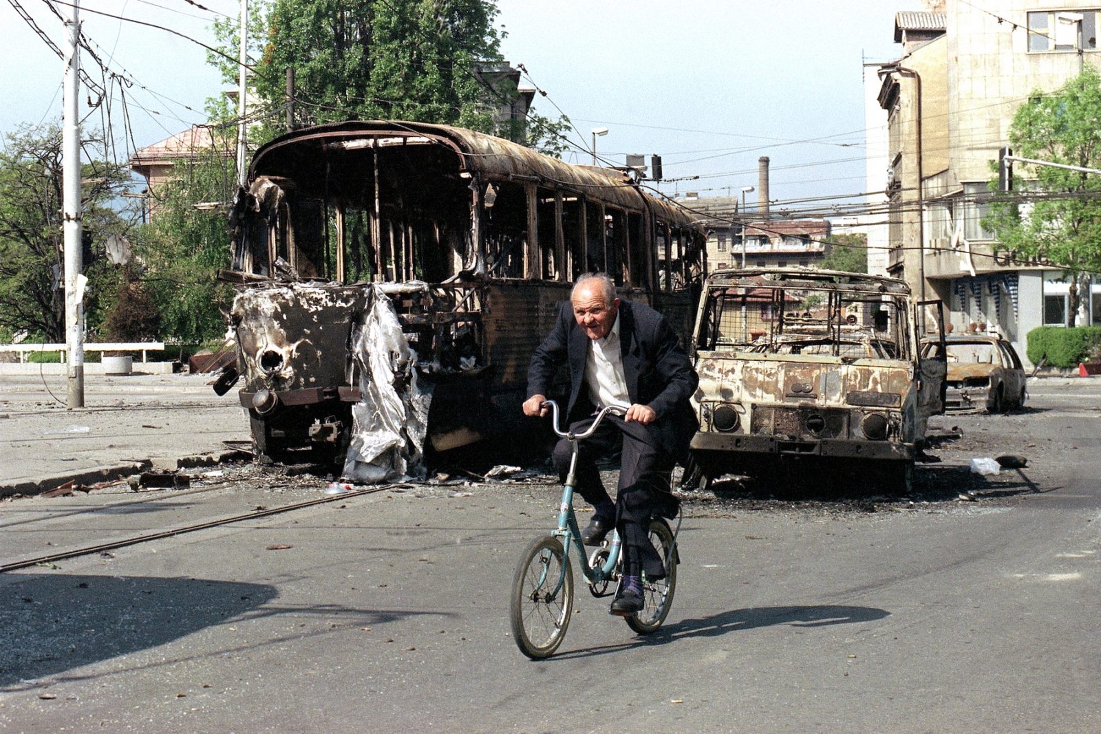 A Sarajevo resident cycles past the wreckage of burnt-out vehicles damaged in fighting last week, in central Sarajevo, May 13, 1992. Sniper fire from the surrounding hills has prevented parts of this town from being cleaned up, but the city was relatively quiet Wednesday as Bosnian Serbs announced unilateral cease fire.