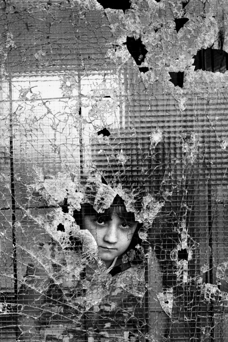Sarajevo, 1992. A small girl stares silently through a shattered window as a United Nations aid convoy reaches besieged people in the Sarajevo suburb of Dobrinja. (Photo By Tom Stoddart/Getty Images)