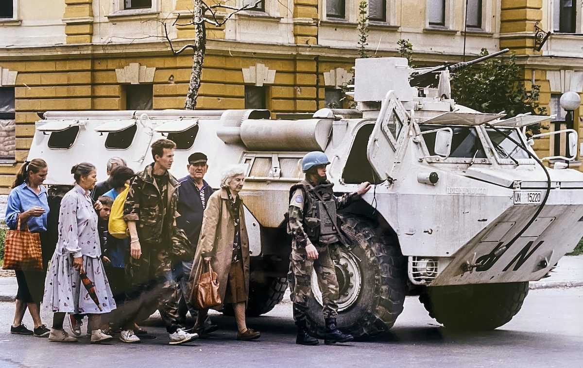 Sarajevan padestrians cross a dangerous street sheltered from snipers by a UN APC.
